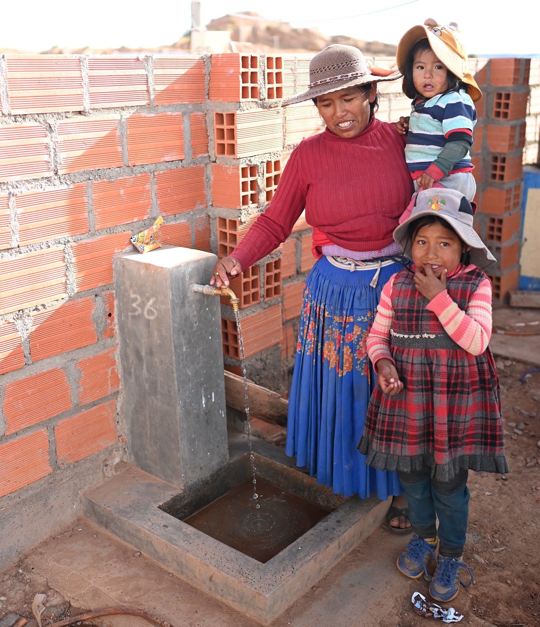 Bolivialaisen perheen äiti kahden lapsen kanssa noutamassa juomavettä.