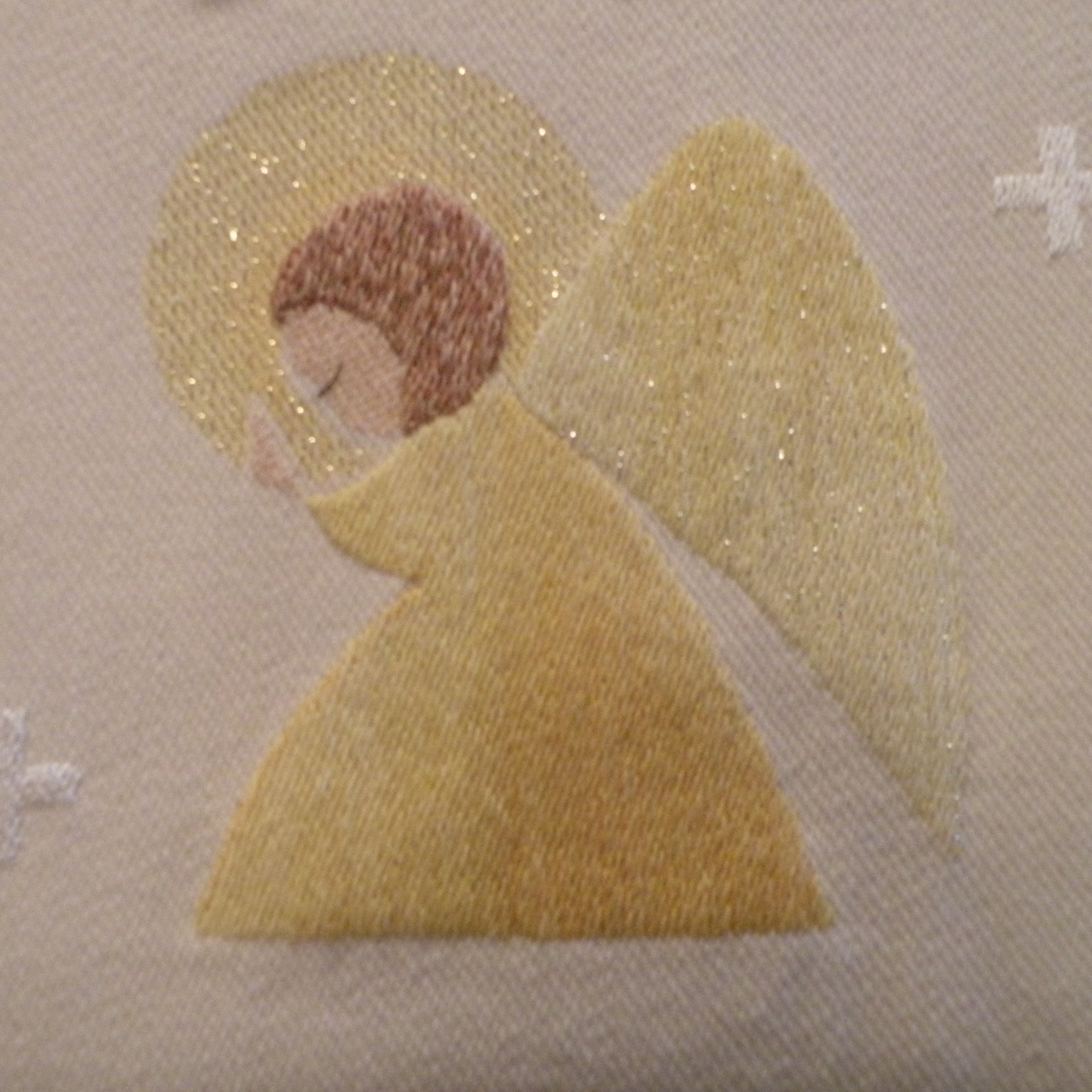 Keltaisista ja kullanhohtoisista langoista kankaaseen punottu ruskeahiuksinen, palvontaan kumartunut enkeli