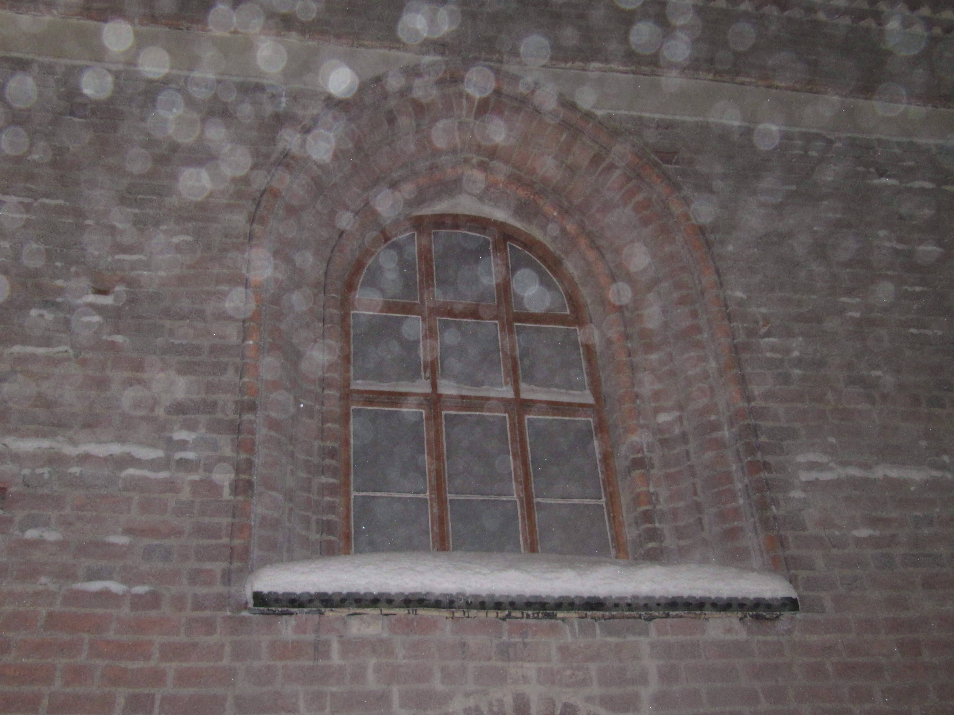 vanhan, tiilestä rakennetun kirkon päätyikkuna ulkoa nähtynä, lumisateessa