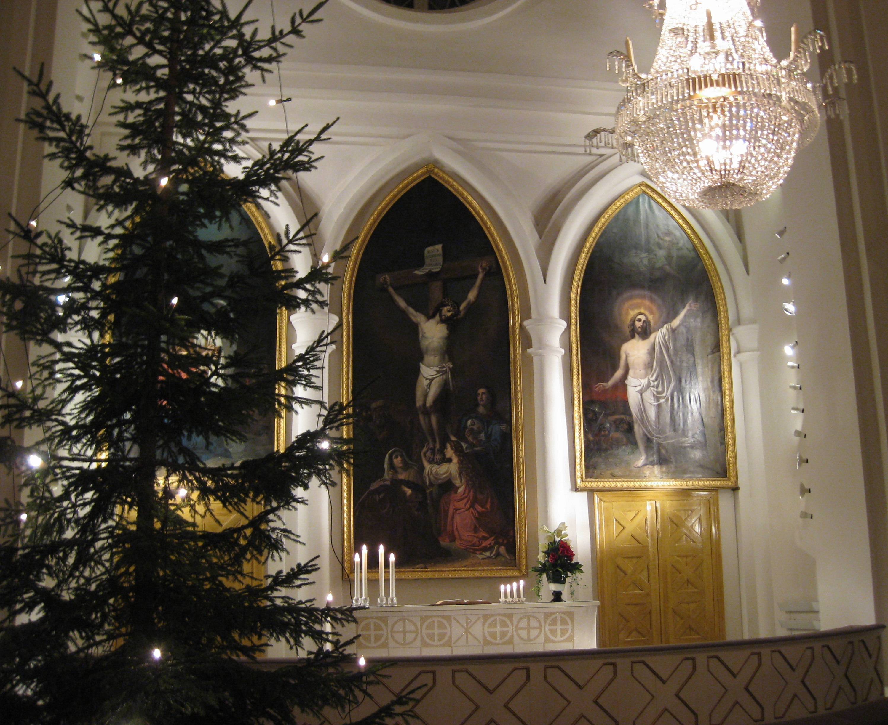 etualalla joulukuusi, taempana voimakkaasti valaistu kirkon alttari suurine alttaritauluineen