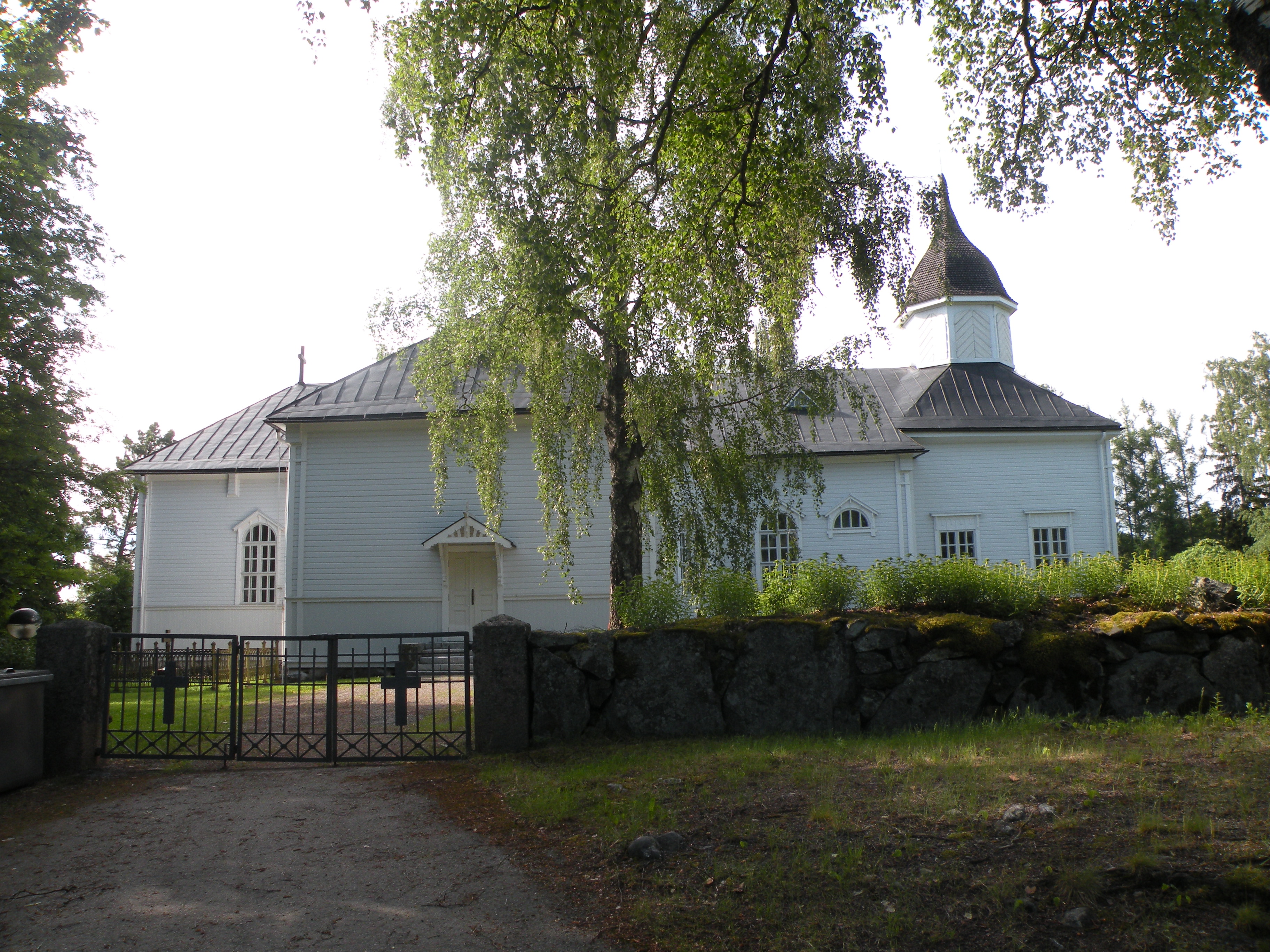 juhannuspäivän messu Kesäinen kuva, jossa Tyrvännön kirkko jää hieman kirkkomaan portilla kasvavan koivun taakse.