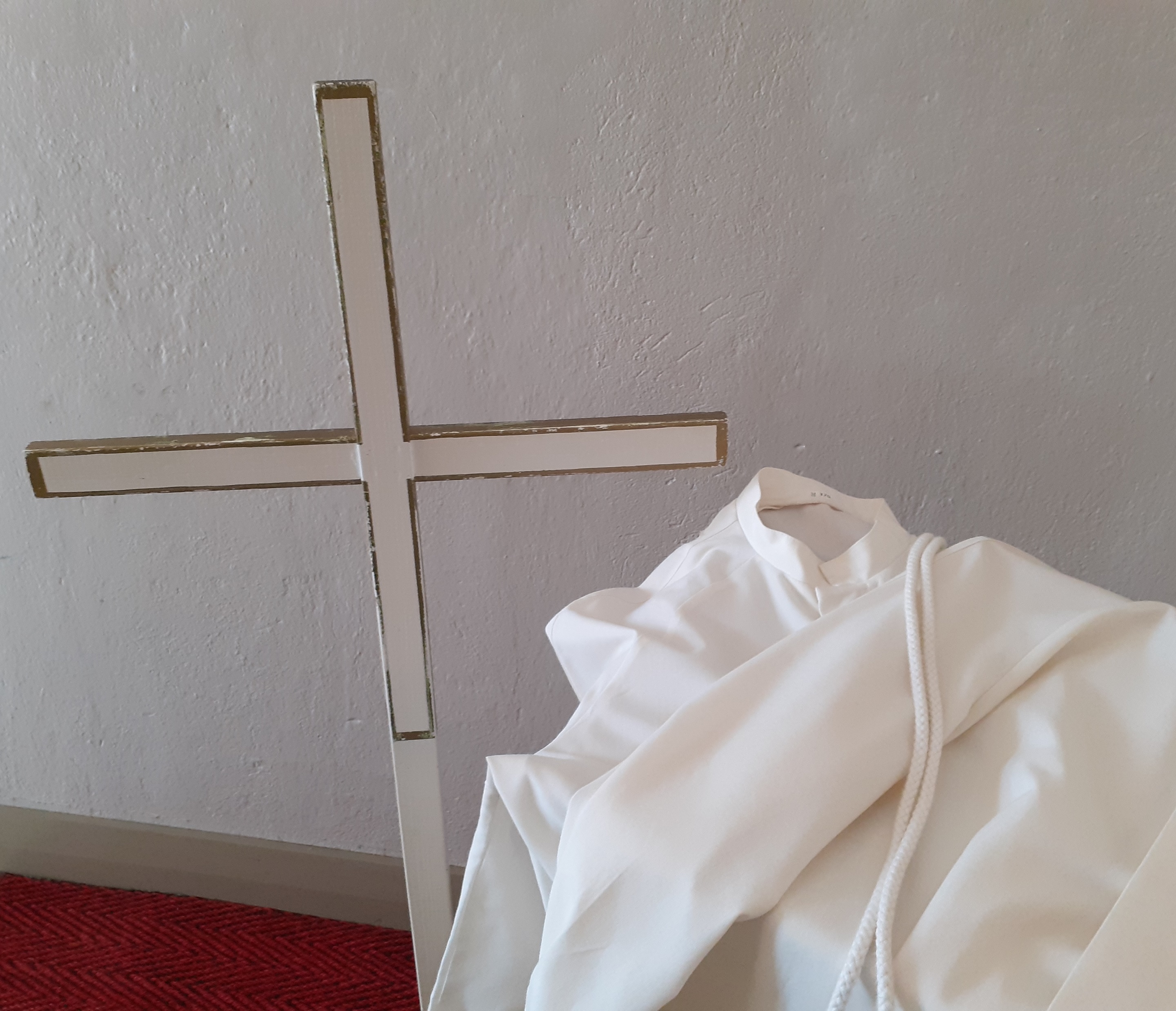 konfirmaatioalboja sekä kulkueessa kannettava puinen risti, taustalla kirkon sisäseinää
